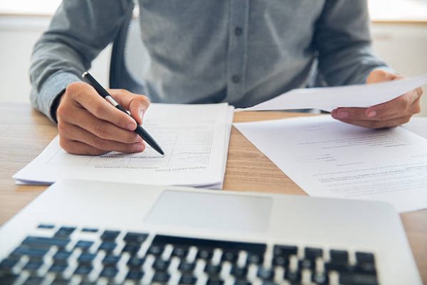 customs clearings Unrecognizable businessman sitting at table holding ballpoint pen and papers and checking documents in office